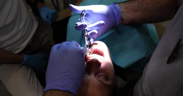 Dentysta w rękawiczkach medycznych wstrzykuje znieczulenie młodej kobiecie ząb w gabinecie dentystycznym. Zastrzyki przeciwbólowe przed zabiegiem stomatologicznym oraz montaż oklein i protez - Materiał filmowy, wideo