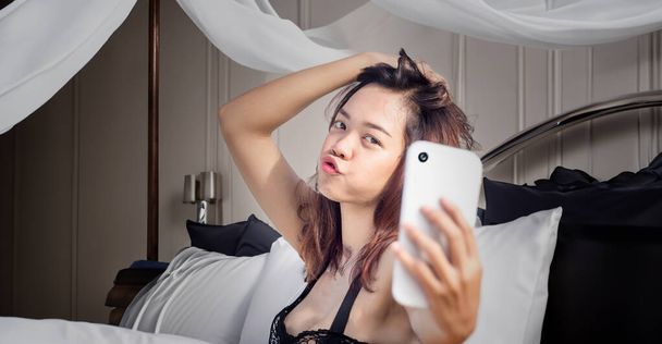 ázsiai lány gyártás szexi szelfi az ágyban telefonnal privát hálószobában tartani titkos emlékek vagy beszélni partner  - Fotó, kép