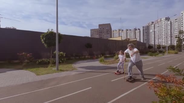 La bambina insegna a un vecchio a cavalcare uno skateboard. Si stanno allenando per cavalcare uno skateboard per strada. Il nonno sta cavalcando uno skateboard. - Filmati, video