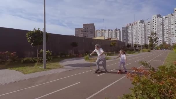 Menina ensina um velho a andar de skate. Eles estão treinando para andar de skate na rua. Avô está montando um skate. - Filmagem, Vídeo