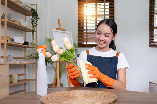 Aziatische vrouwelijke huishoudster schoonmaken van het huis met behulp van spray en schoonmaakdoek aan de tafel in de woonkamer. - Foto, afbeelding