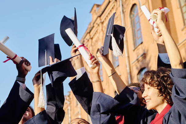 Bir grup mutlu öğrenci diplomalarıyla ellerini kaldırarak üniversiteyi bitiriyor. - Fotoğraf, Görsel