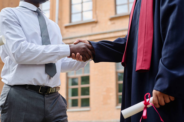 Primer plano del profesor afroamericano estrechando la mano con el estudiante, lo felicitó con la graduación - Foto, Imagen
