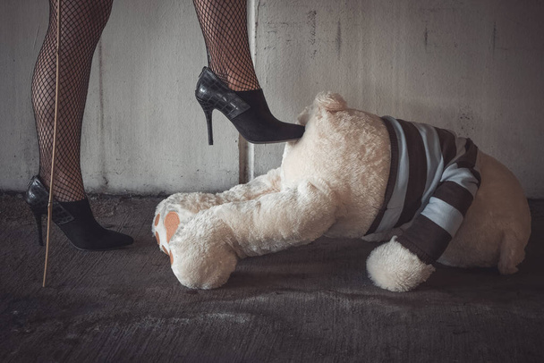 a woman in black high heels gives a teddy bear a kick in the butt - Zdjęcie, obraz