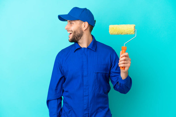Painter caucasian man isolated on blue background laughing in lateral position - Photo, Image