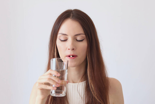 Egy gyönyörű fiatal nő tablettákat, vitaminokat és badákat iszik, és lemossa őket egy pohár vízzel.. - Fotó, kép