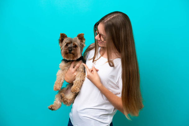 Nuori liettualainen nainen pitelee sinisellä pohjalla eristettyä koiraa ja osoittaa sillä - Valokuva, kuva