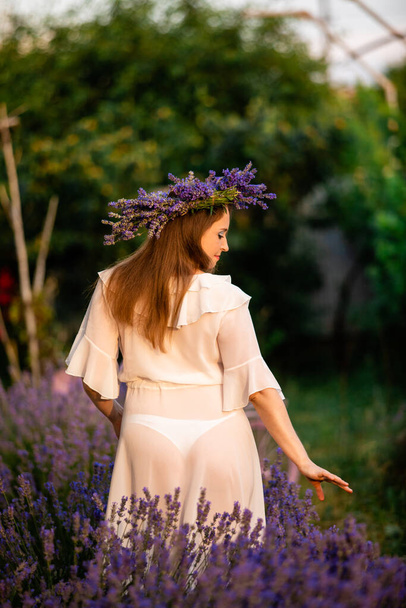 Woman in lavender wreath and whitre dress on the lavender field. Girl collects lavender. - Photo, image