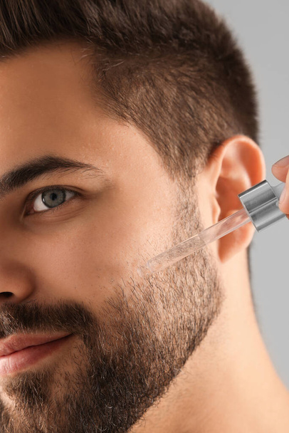 Handsome man applying cosmetic serum onto face, closeup - Фото, изображение