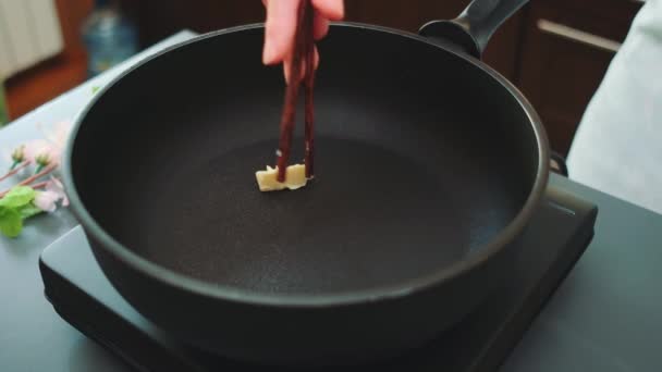 Жіночі руки кладуть шматочок масла на сковороду з бамбуковими паличками. Середній знімок кухонного столу. Кулінарія на кухні - Кадри, відео
