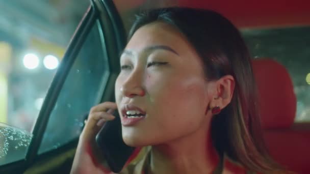 Primer plano de la joven mujer asiática mirando la ciudad nocturna a través de la ventana abierta y hablando por teléfono móvil durante el viaje - Metraje, vídeo