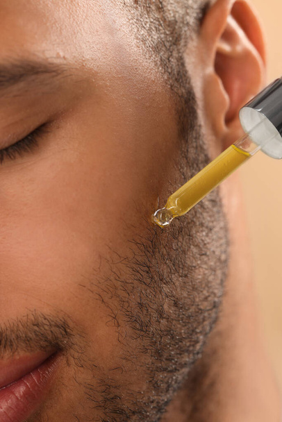 Man applying cosmetic serum onto face, closeup - Фото, изображение