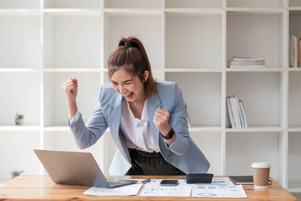 Mujeres de negocios asiáticas muestran alegre expresión de éxito en el trabajo sonriendo felizmente con un ordenador portátil en una oficina moderna.. - Foto, imagen