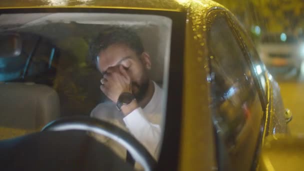 Втомлений бізнесмен натирає шию і обличчя, а потім спирається на кермо, сидячи в машині в дощову ніч - Кадри, відео