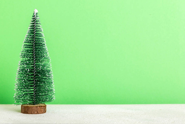 Ένα μικρό χριστουγεννιάτικο δέντρο σε έγχρωμο φόντο. διακόσμηση νέου έτους με χώρο αντιγραφής. - Φωτογραφία, εικόνα