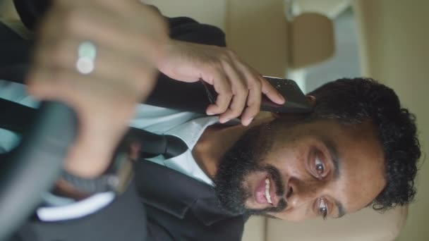 Κάθετη λήψη επαγγελματία επιχειρηματία με επίσημο κοστούμι κάθεται στη θέση του οδηγού στο αυτοκίνητο, κρατώντας τιμόνι και μιλώντας στο κινητό τηλέφωνο - Πλάνα, βίντεο