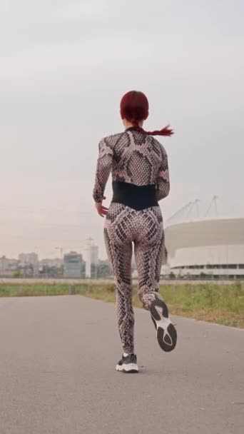 Vertical Video, Slim Athletic Woman with Red Hair in Sports Overalls Run. Girl Athlete is Engaged in Jogging Outdoors in the Daytime. Female Runner Trains by Running. Slow Motion. - Footage, Video