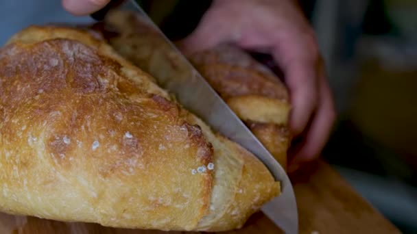 Цілий зерновий хліб покласти на кухонну дерев'яну тарілку з шеф-кухарем, який тримає золотий ніж для різання. Свіжий хліб на столі крупним планом. Свіжий хліб на кухонному столі Здорове харчування та традиційна концепція пекарні - Кадри, відео