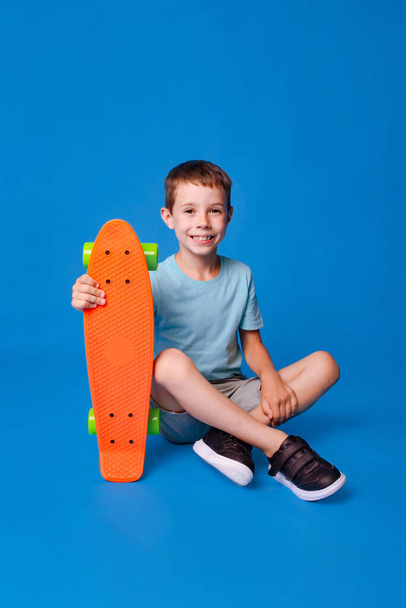 feliz sorrindo menino em azul mockup T-shirt segurando skate isolado em luz azul estúdio fundo - Foto, Imagem