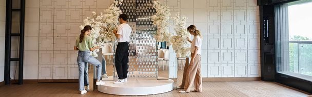 творческий коллектив флористов, организующих декоративную праздничную композицию в просторном зале мероприятий, баннере - Фото, изображение