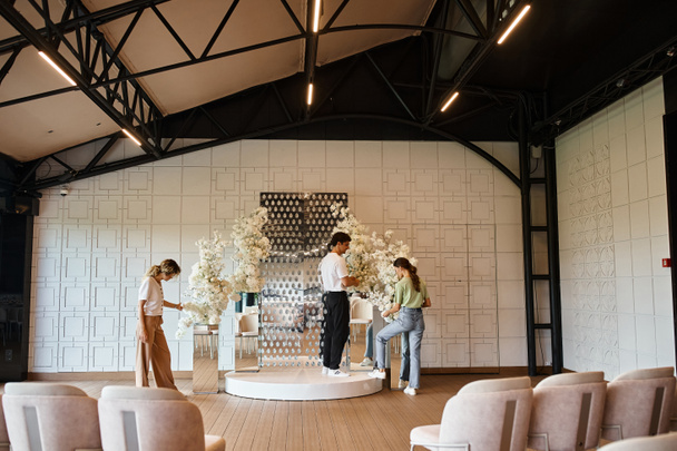 équipe créative de concepteurs d'événements préparant salle de fête moderne en arrangeant la composition florale - Photo, image