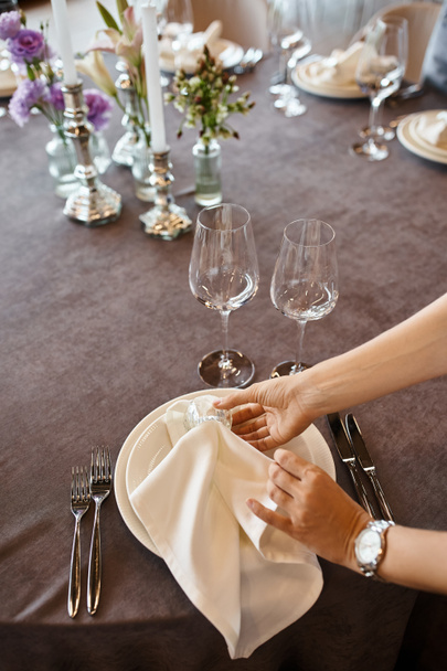 vista ritagliata del decoratore che tiene i tovaglioli vicino ai piatti sul tavolo con impostazione festiva, impostazione dell'evento - Foto, immagini