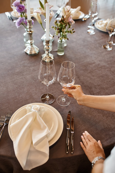 cropped view of event decorator holding glass near table with festive setting, banquet setup - Photo, Image