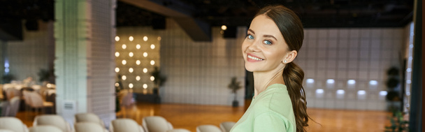 cheerful creative female decorator looking at camera in spacious and modern event hall, banner - Photo, Image