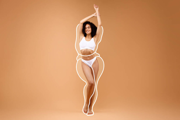 Körpermodellierung. Junge sportliche Afroamerikanerin in Unterwäsche mit gezeichneten Umrissen um die Figur, beiger Hintergrund. Schöne Dame demonstriert Ergebnis von Gewichtsverlust, Collage mit Kopierraum - Foto, Bild
