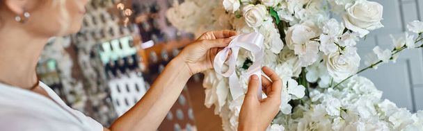 cropped view of decorator tying ribbon on white floral composition in festive event hall, banner - Photo, Image