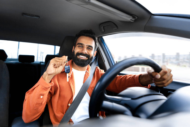 Kendi otomobilimiz var. Gururlu araba sahibi Hintli adam yeni otomobil anahtar sürücü aracını gösteriyor, sürücü koltuğunda elleri direksiyonda oturuyor, kameraya gülümsüyor. Hayaller gerçek olur. - Fotoğraf, Görsel