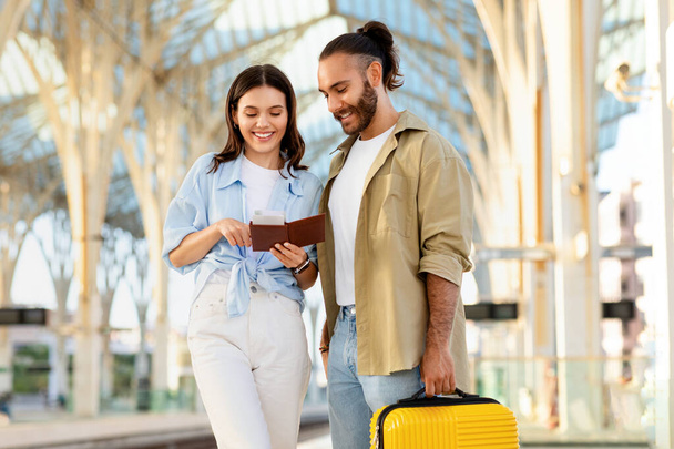 Couple caucasien millénaire positif avec valise regarde passeport à la gare. Voyager ensemble, relations et romance, style de vie de voyage, vacances d'été et visite - Photo, image