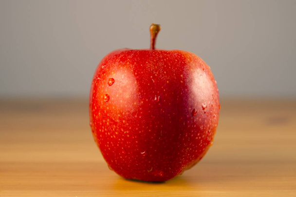 Κόκκινο μήλο με σταγόνες νερού στο ξύλινο τραπέζι. Ρηχό βάθος πεδίου - Φωτογραφία, εικόνα