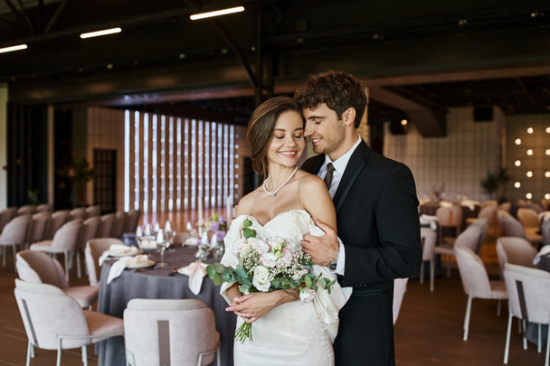 pareja encantada en elegante traje de novia sonriendo a la cámara en la sala de banquetes moderna, pancarta - Foto, imagen