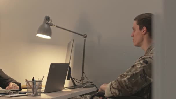 Πλευρική άποψη μέσο πλάνο του αναπηρικού αμαξιδίου νεαρός καυκάσιος στρατιώτης με στολή καμουφλάζ έχοντας συνεδρία θεραπείας με ειδικό ψυχίατρο στο άνετο γραφείο - Πλάνα, βίντεο