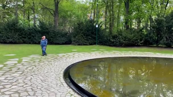 The Memorial to the Sinti and Roma Victims of National Socialism on Simsonweg in the Tiergarten in Berlin (en inglés). Consiste en una piscina oscura y circular en el centro de la cual hay una piedra triangular. - Imágenes, Vídeo