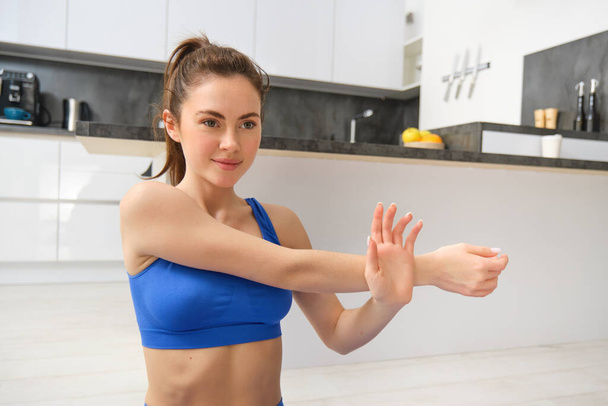 Mujer joven hace ejercicio desde casa, se sienta en la esterilla de yoga y estira las manos, sesión de entrenamiento de fitness en la sala de estar. - Foto, imagen