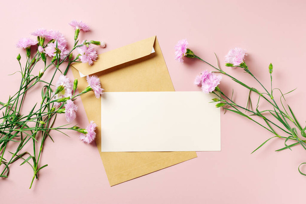 Λευκά ευχετήρια κάρτα και όμορφα άνθη γαρύφαλλου στο ροζ φόντο. - Φωτογραφία, εικόνα
