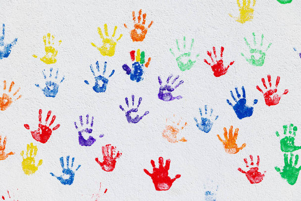 O teste padrão das mãos coloridas foi carimbado em uma parede branca com as mãos coloridas das crianças - Foto, Imagem