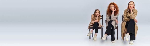 female generations, happy redhead women and child sitting in row on chairs on grey backdrop - 写真・画像