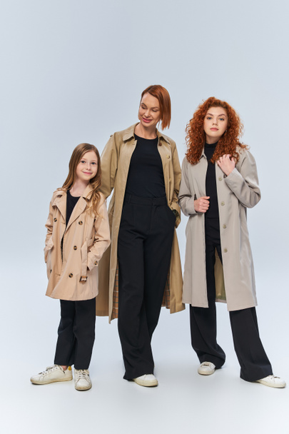 redhead family in trench coats posing together on grey background, three generations of women - Φωτογραφία, εικόνα
