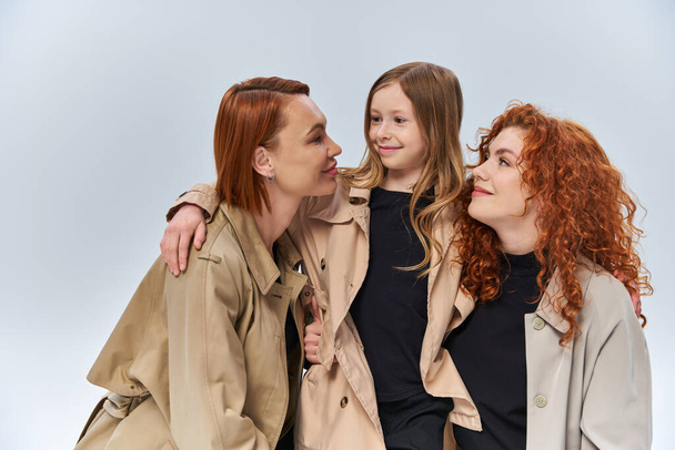 cute redhead girl hugging happy women in autumn coats on grey background, female generations - Photo, Image