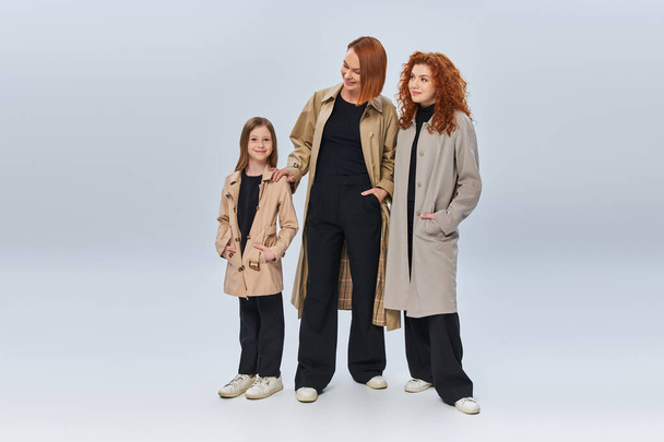 zrzka rodina v podzimních kabátech pózuje s rukama v kapsách na šedém pozadí, tři generace - Fotografie, Obrázek