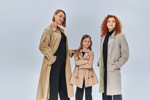 familia pelirroja de tres generaciones posando juntos en abrigos de otoño sobre fondo gris, moda de otoño - Foto, Imagen