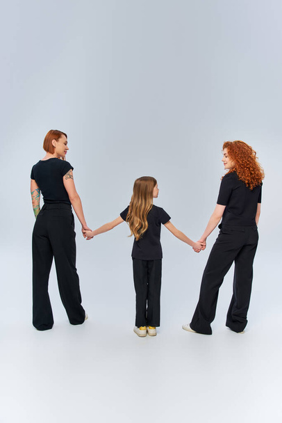 weibliche Generationen, glückliche rothaarige Familie Händchen haltend und in passender Kleidung auf grau - Foto, Bild