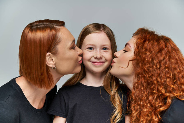 female generations concept, redhead women kissing cheeks of freckled girl on grey background - Photo, Image