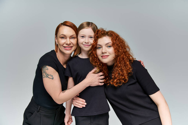 家族の肖像画,赤毛の女性および灰色の背景の笑顔のマッチングの服装の解体された少女 - 写真・画像