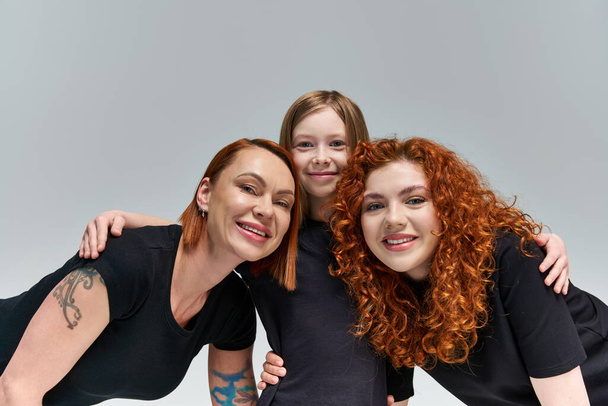 family portrait, happy freckled girl hugging redhead women in matching attire  on grey background - Photo, Image