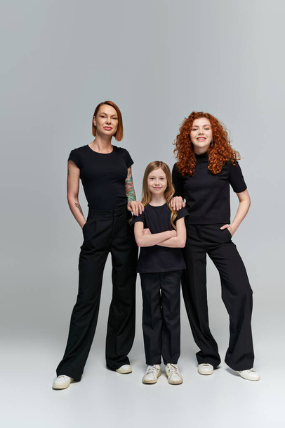 retrato de família, três gerações de mulheres em roupas correspondentes em pé sobre fundo cinza - Foto, Imagem