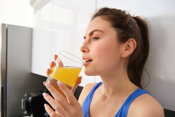Mulher bonita bebendo um suco de laranja orgânico. Ajuste a mulher jovem que bebe do vidro. Menina saudável desfrutar de bebida de desintoxicação e olhando para longe. - Foto, Imagem